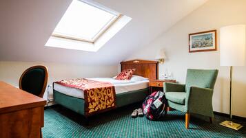 Een hotelkamer met een bed, een bureau, een stoel, een lamp en een dakraam.