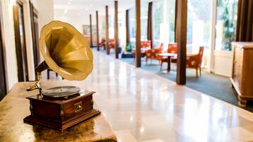 A vintage gramophone on a wooden table in a well-lit hallway with modern chairs and tables in the background.