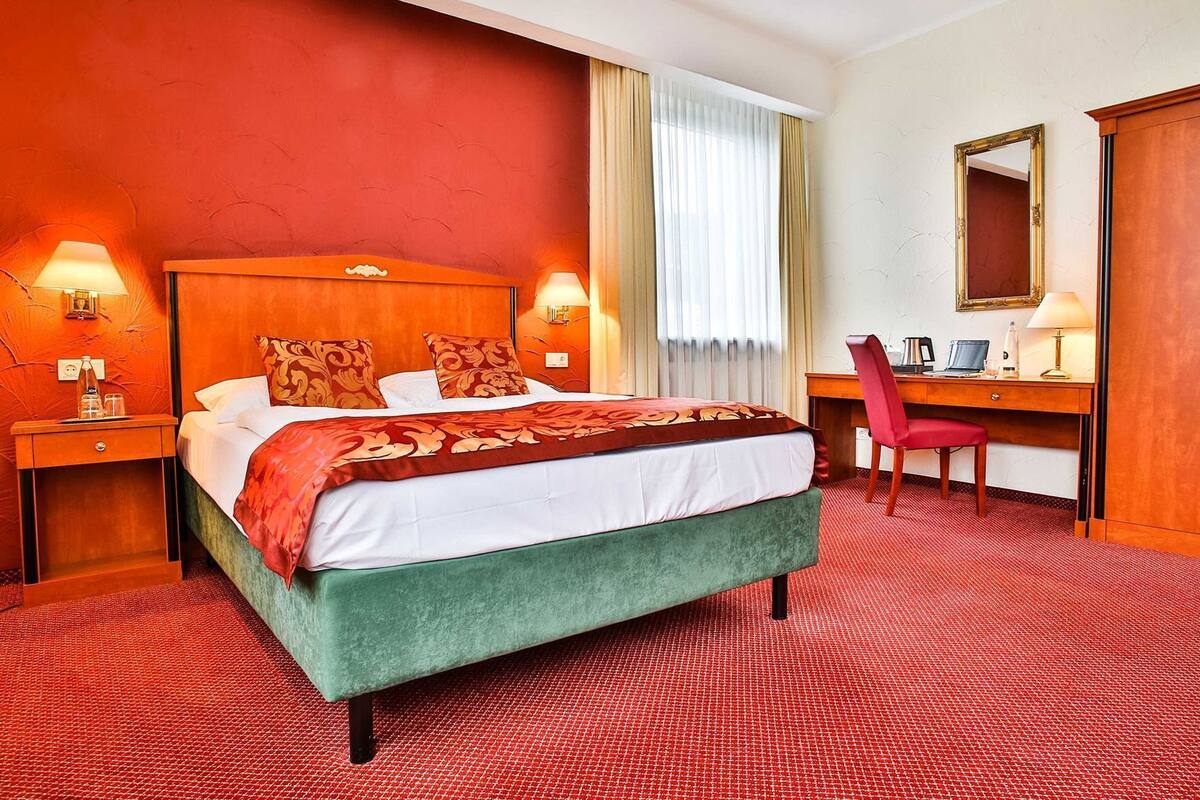 Ett hotellrum med en säng, ett skrivbord, en stol, en spegel och ett fönster med gardiner.