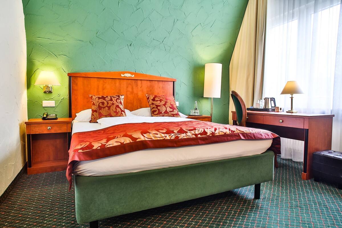 Ett hotellrum med en säng, sängbord, ett skrivbord, en stol och en resväska.