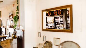 A room with a mirror reflecting a bar area, shelves with bottles, and a wall-mounted clock.