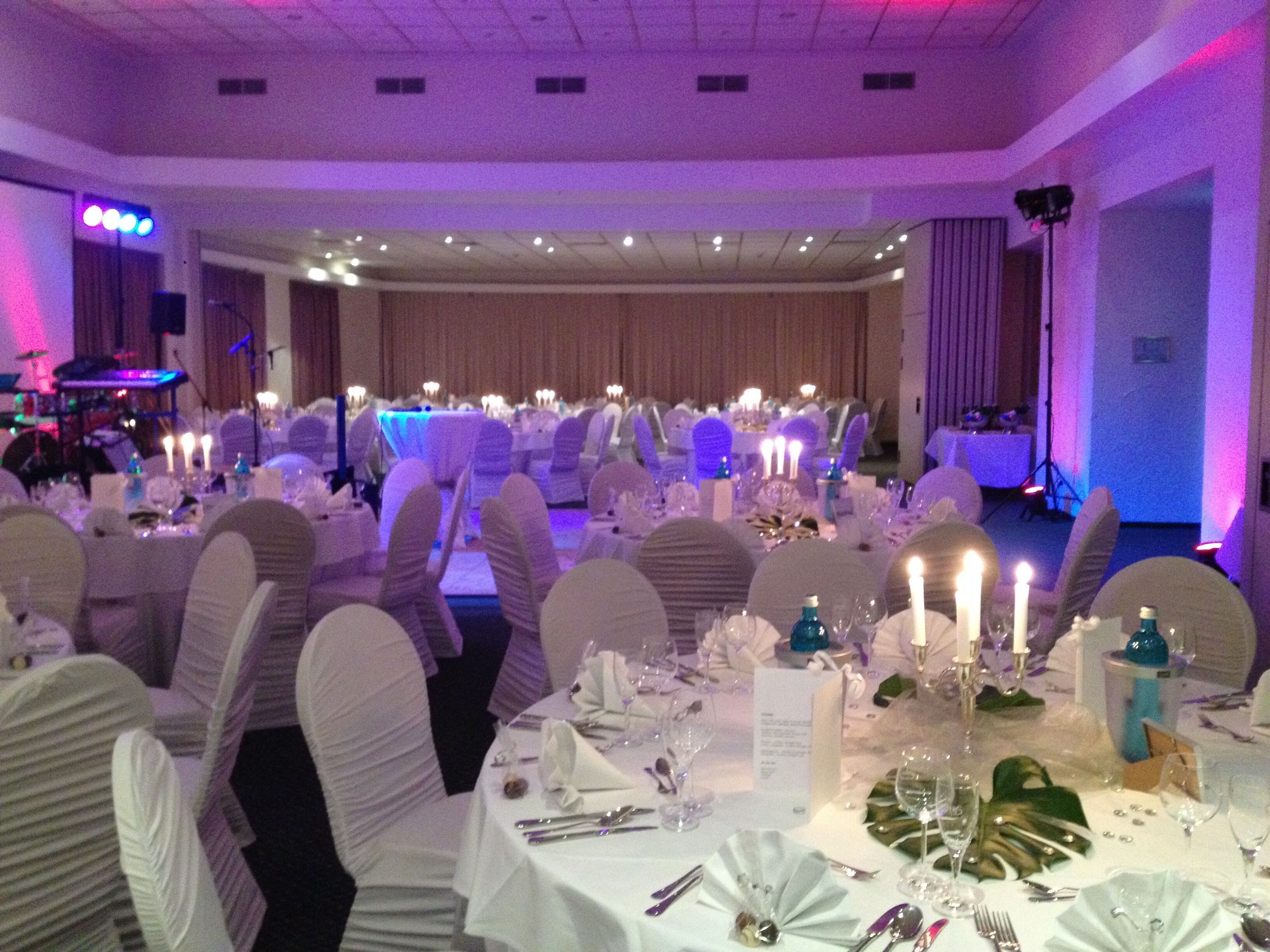 Un salón de banquetes con mesas redondas dispuestas para un evento formal, con manteles blancos, velas y cubertería cuidadosamente organizada.
