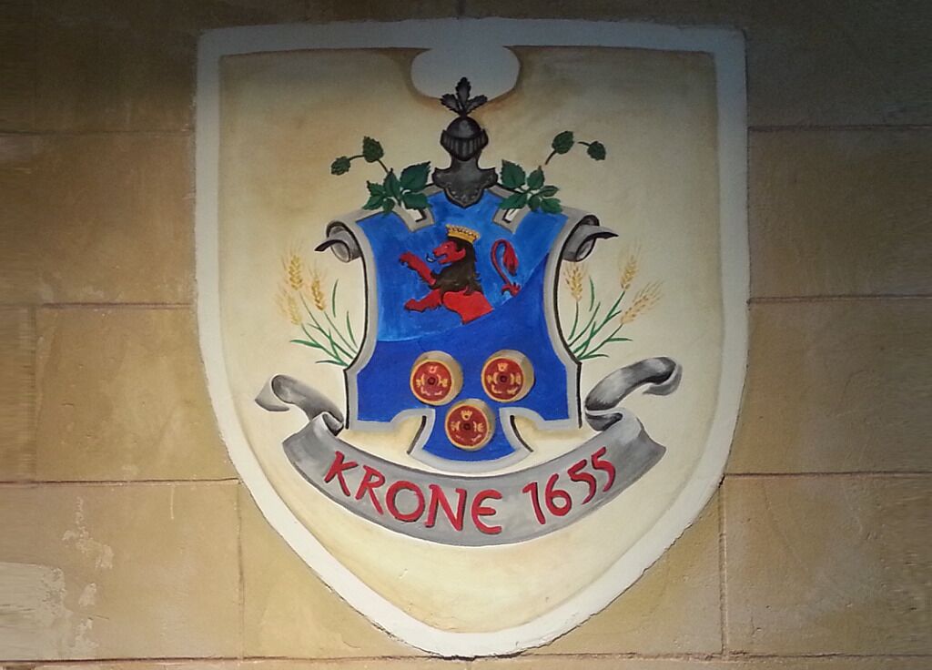A heraldic shield with a crest and the inscription "KRONE 1655" on a wall.