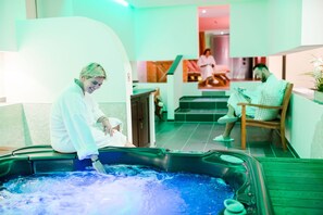 Un espace spa avec un jacuzzi, une personne en peignoir et une autre personne qui lit un livre.