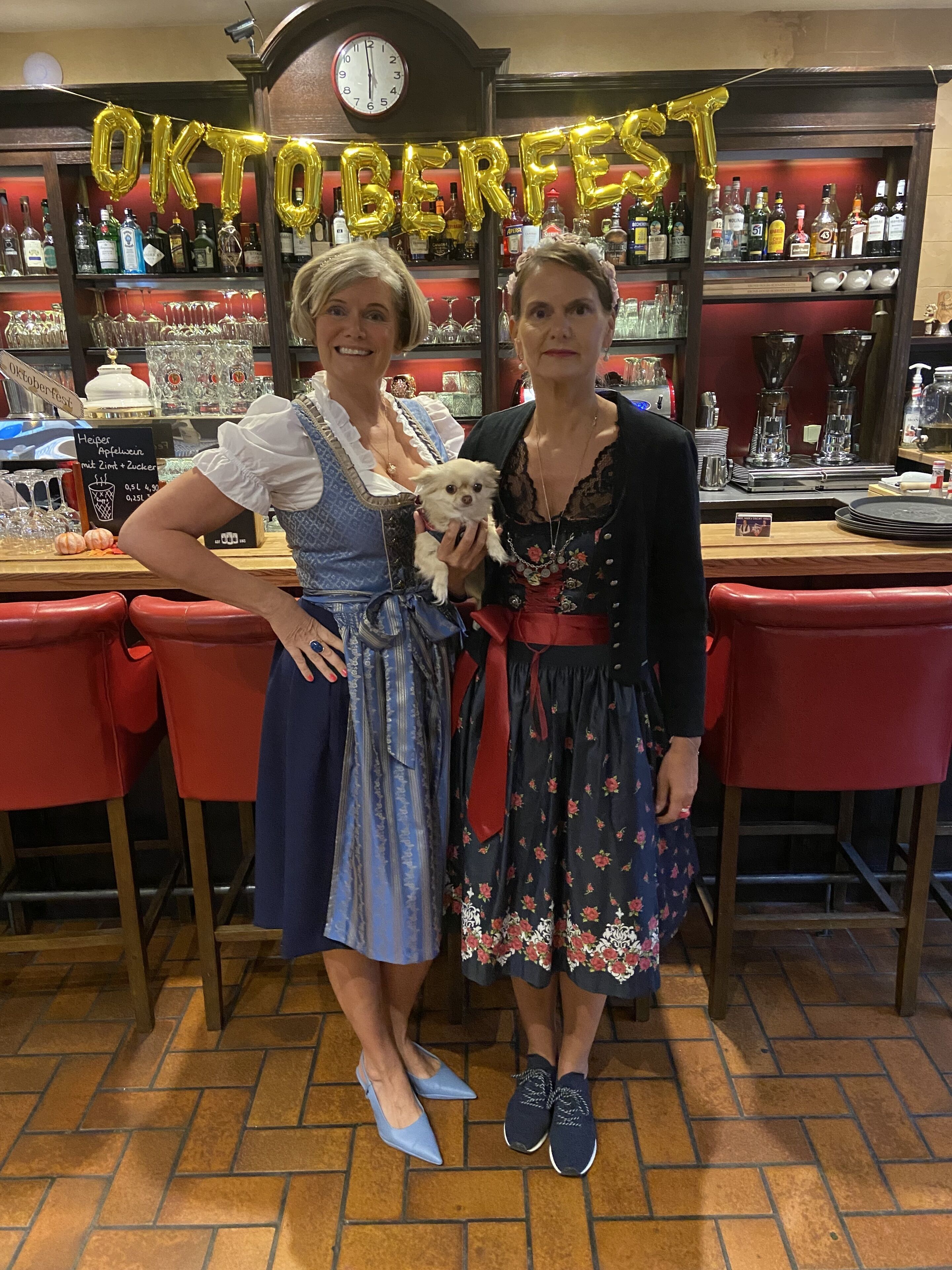 Dos personas con vestimenta tradicional en un bar, con un letrero que dice "Oktoberfest".