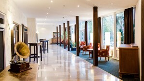 Et hotel lobby med en lang gang, træsøjler og forskellige siddeområder.