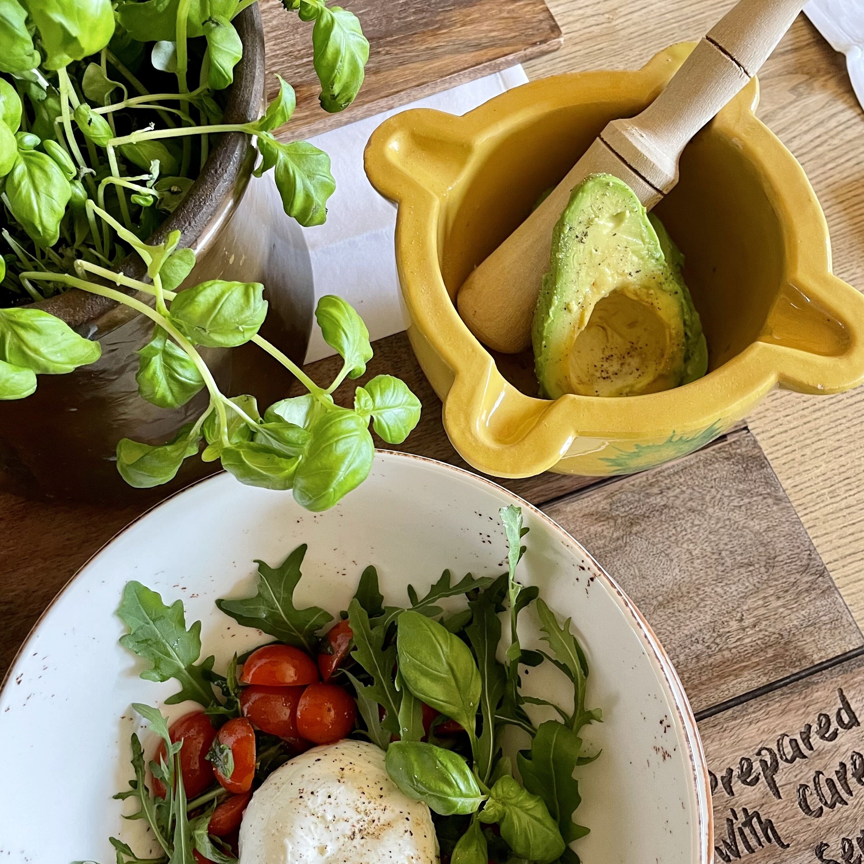 Une assiette de salade composée de roquette, de tomates cerises et d’un œuf poché, un bol de jeunes pousses et un bol en bois contenant un avocat.