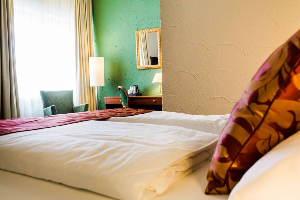 Ett hotellrum med en säng, ett skrivbord med en lampa, en stol och en spegel på väggen.