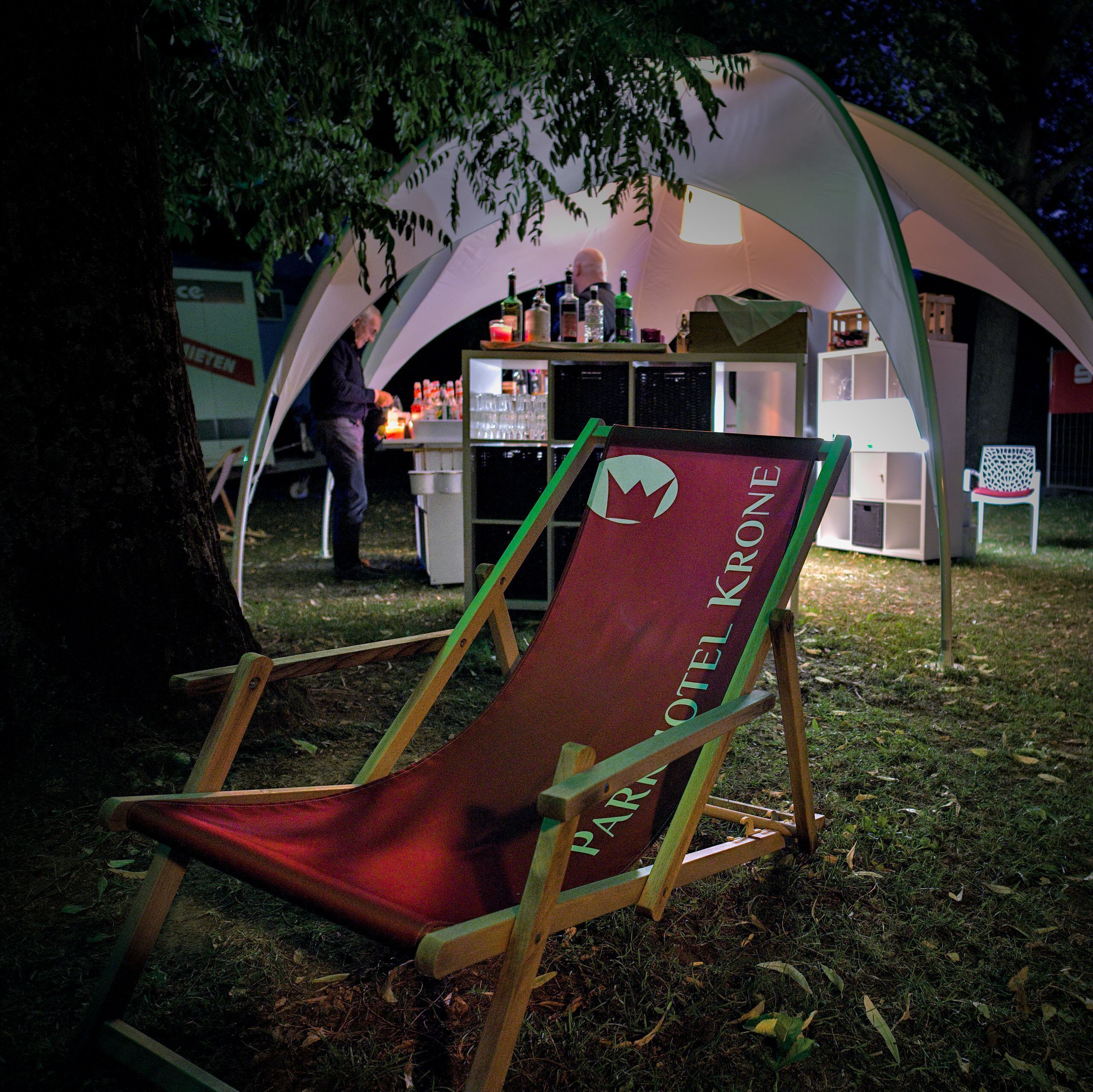 A tent with a bar area, a folding chair, and a sign with the text "HOTEL KRONE".