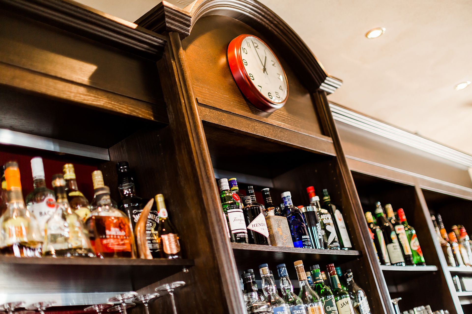 Un espace bar avec des étagères remplies de différentes bouteilles d’alcool et une horloge au-dessus.