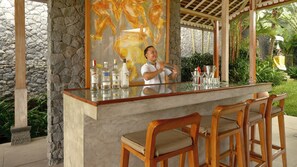 A bar area with a stone wall backdrop, wooden chairs, and a variety of bottles. - Mannao Estate by Villa Finder (Kerobokan)