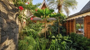 A tropical garden with a stone wall, various plants, and a wooden structure. - Mannao Estate by Villa Finder (Kerobokan)