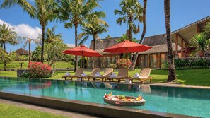 A pool area with lounge chairs and umbrellas, surrounded by palm trees and a building with a tiled roof. - Mannao Estate by Villa Finder (Kerobokan)
