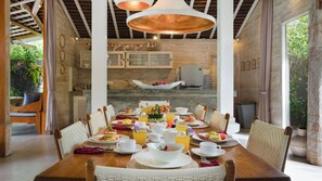 A dining area with a wooden table set for breakfast, featuring plates of food, drinks, and a variety of tableware. - Mannao Estate by Villa Finder (Kerobokan)