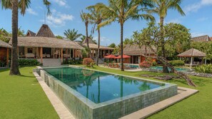 A resort with a swimming pool, palm trees, and thatched-roof structures.