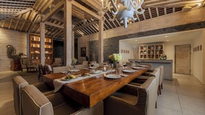 A spacious dining area with a long wooden table, multiple chairs, and a stone accent wall. - Mannao Estate by Villa Finder (Kerobokan)