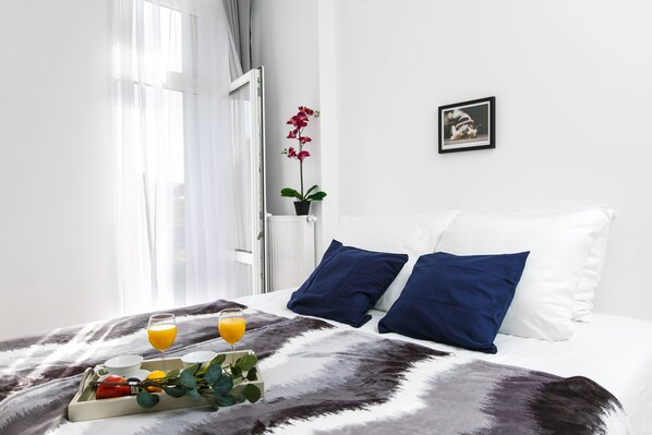 Una cama bien hecha con almohadas azules y blancas, una bandeja con alimentos para el desayuno y una planta en maceta.