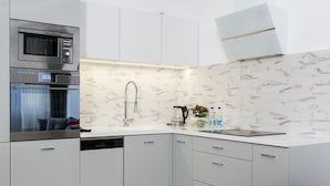 A modern kitchen with white cabinetry, a built-in oven, a stainless steel faucet, and a marble backsplash. - Otium Old Town Łobzowska (Kraków)