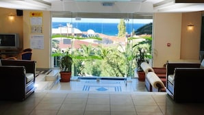 A hotel lobby with a view of the sea, potted plants, and seating areas.