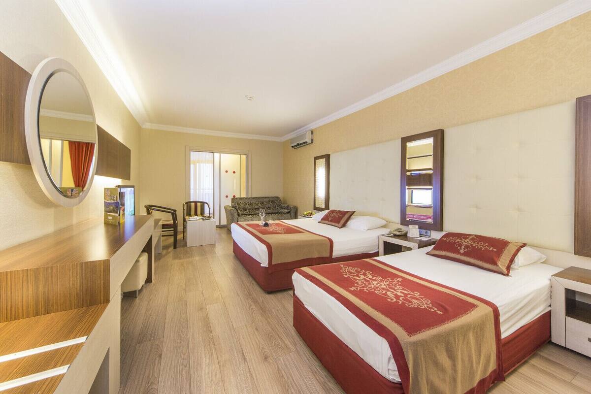 A hotel room with two beds, a desk, a chair, a mirror, and a window.