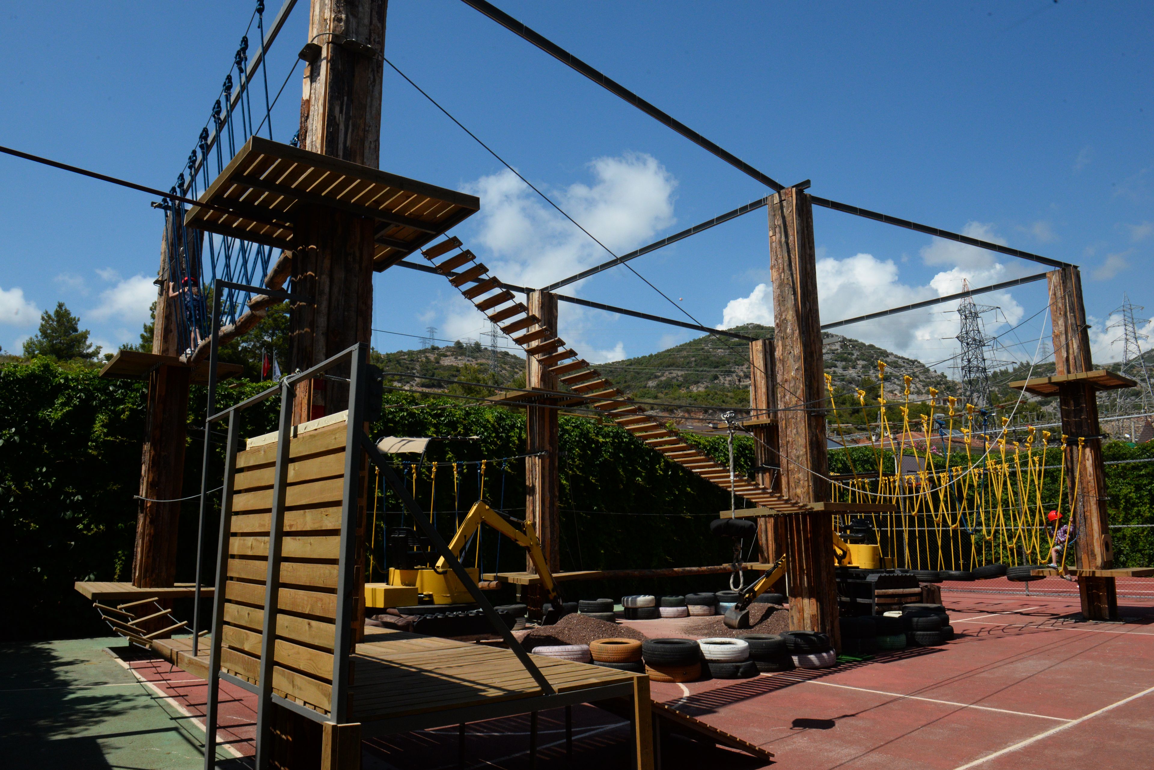 An outdoor adventure park with wooden climbing structures, a zip line, and a tire obstacle course.