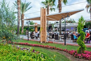 Un espace extérieur aménagé avec des tables et des chaises, entouré de palmiers et de plantes en fleurs.