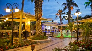 Un área de restaurante al aire libre con mesas y sillas, rodeada de palmeras y flores.