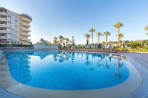 A swimming pool with a clear blue water surface, surrounded by lounge chairs and palm trees. - Beach Club Doganay (Alanya)