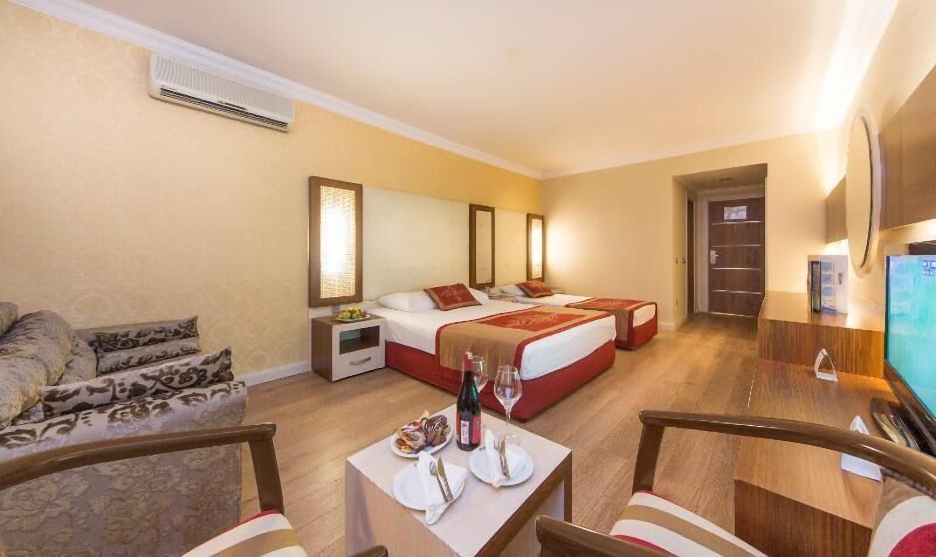 A hotel room with a bed, bedside tables, a TV, a desk with chairs, and a sofa.