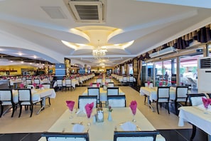 A spacious restaurant with multiple dining tables and chairs, a chandelier, and air conditioning units. - Beach Club Doganay (Alanya)