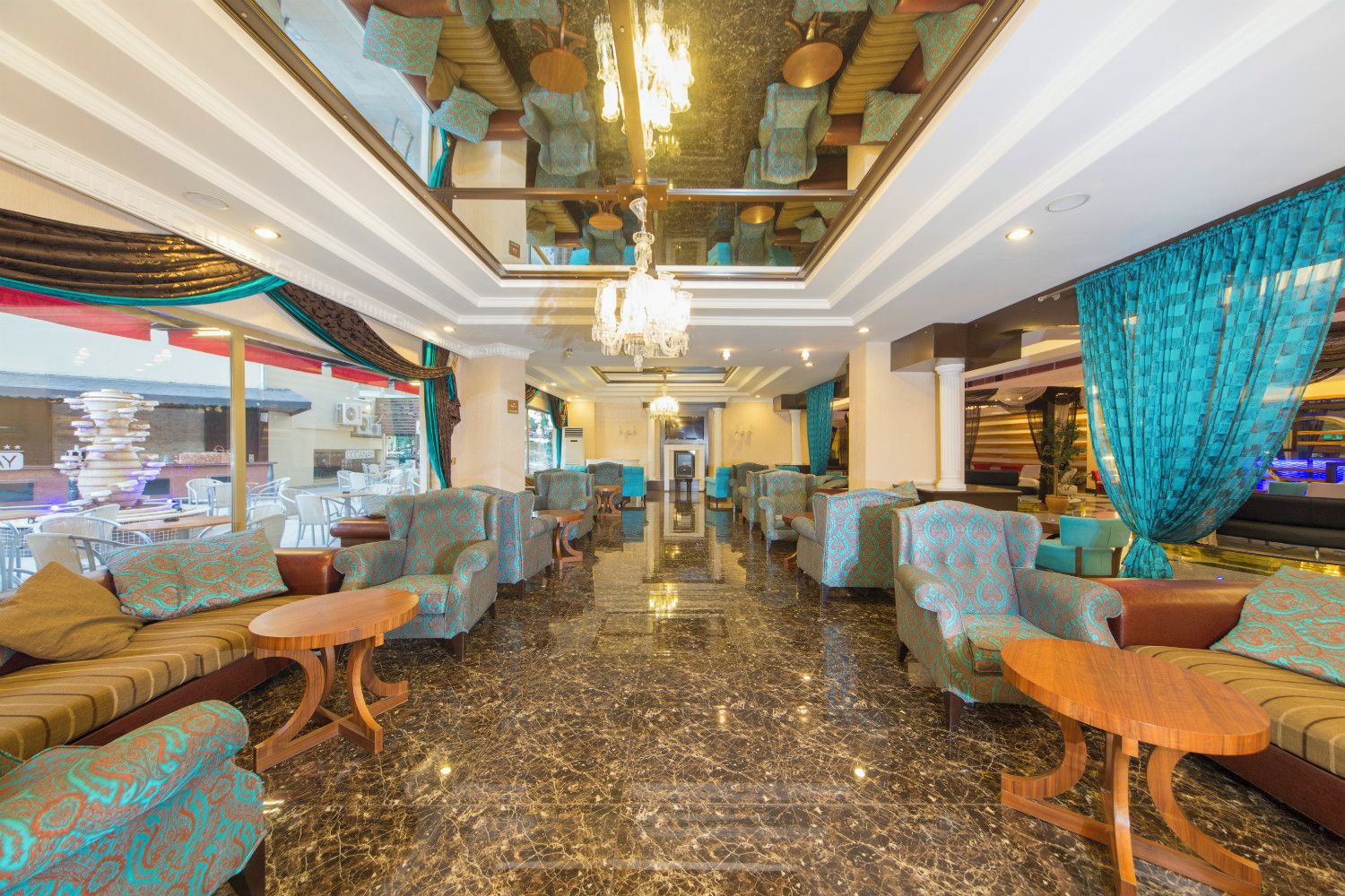 A hotel lobby with patterned sofas, a chandelier, and a view of the outside.