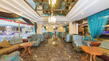 A hotel lobby with patterned sofas, a chandelier, and a view of the outside.