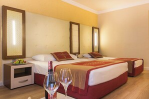 A hotel room with two beds, a bedside table with a fruit bowl, and two wine glasses.