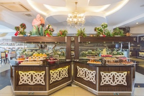 A buffet area with multiple food stations, decorative floral arrangements, and a chandelier. - Beach Club Doganay (Alanya)