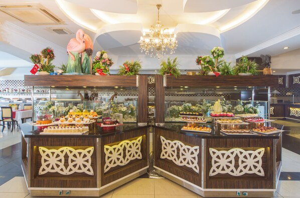 A buffet area with multiple food stations, decorative floral arrangements, and a chandelier. - Beach Club Doganay (Alanya)