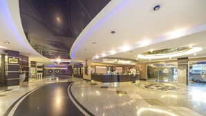 Un moderno vestíbulo de hotel con un diseño de piso curvo, una recepción y un techo con un despliegue de luces que simula estrellas.