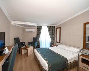 A hotel room with a bed, a desk with a computer, a chair, a TV, and a window with curtains. - Beach Club Doganay (Alanya)