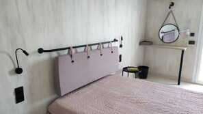 A bedroom with a bed, a headboard with hooks, a bedside table, a mirror, and a small stool.