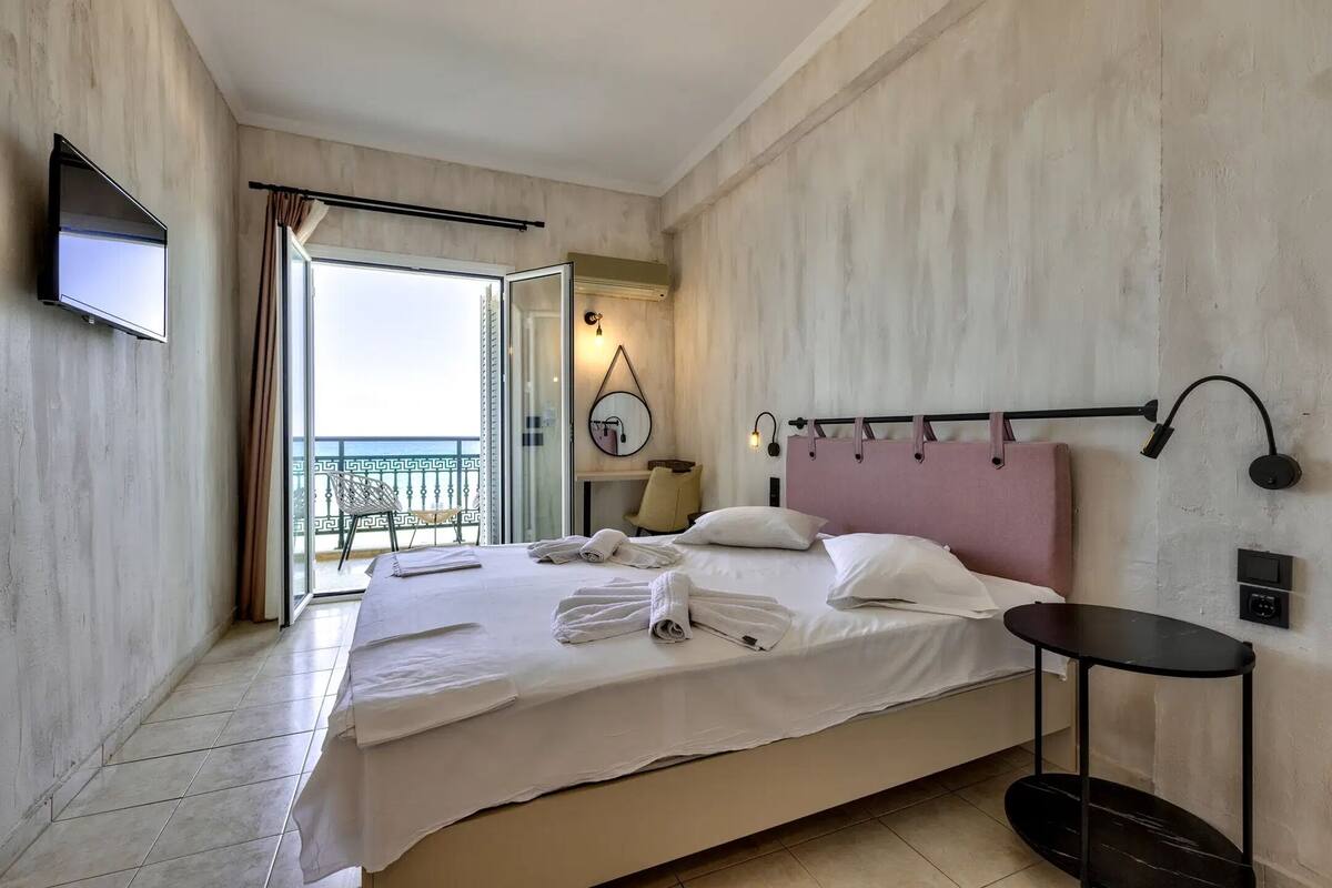 A hotel room with a bed, a TV, a bedside table, and a view of the outside.