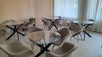 A conference room with glass tables and modern chairs, a potted plant, and a large window with curtains.