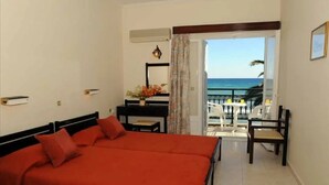 A hotel room with a bed, a desk, a chair, and a view of the sea.