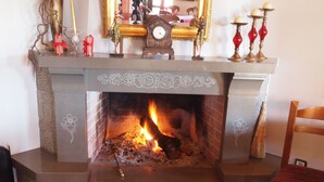 A fireplace with a fire, a clock, and decorative items on the mantel. - Archontiko Tzoumerkon (Central Tzoumerka)