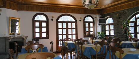 Un comedor con mesas y sillas de madera, ventanas arqueadas y una araña.