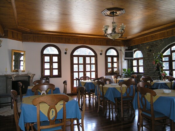 A dining area with wooden tables and chairs, arched windows, and a chandelier.
