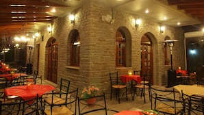 An indoor dining area with stone walls, wooden beams, and tables with red tablecloths. - Archontiko Tzoumerkon (Central Tzoumerka)
