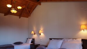 A bedroom with a sloped ceiling, wooden beams, a chandelier, two bedside lamps, and a bed with white linens and multiple pillows. - Archontiko Tzoumerkon (Central Tzoumerka)