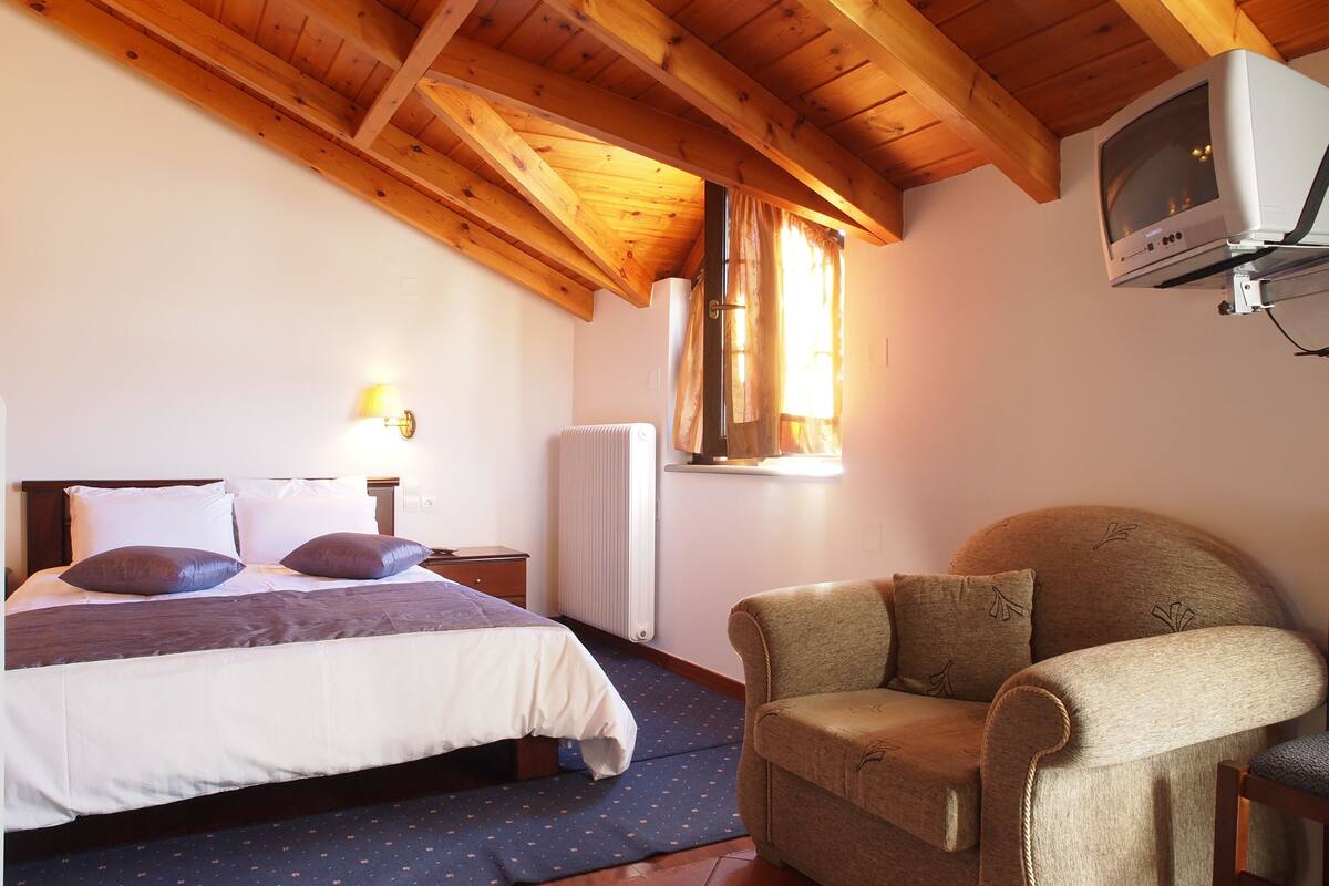 Een slaapkamer met een bed, een stoel, een televisie en een raam met gordijnen.