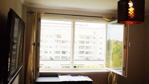 A bedroom with a large window, a bed, a desk, and a hanging light fixture. - Central - 2 Bedroom Apartment (Sollentuna)