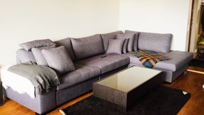 A modern living room with a grey sectional sofa, a glass coffee table, and a black rug. - Central - 2 Bedroom Apartment (Sollentuna)