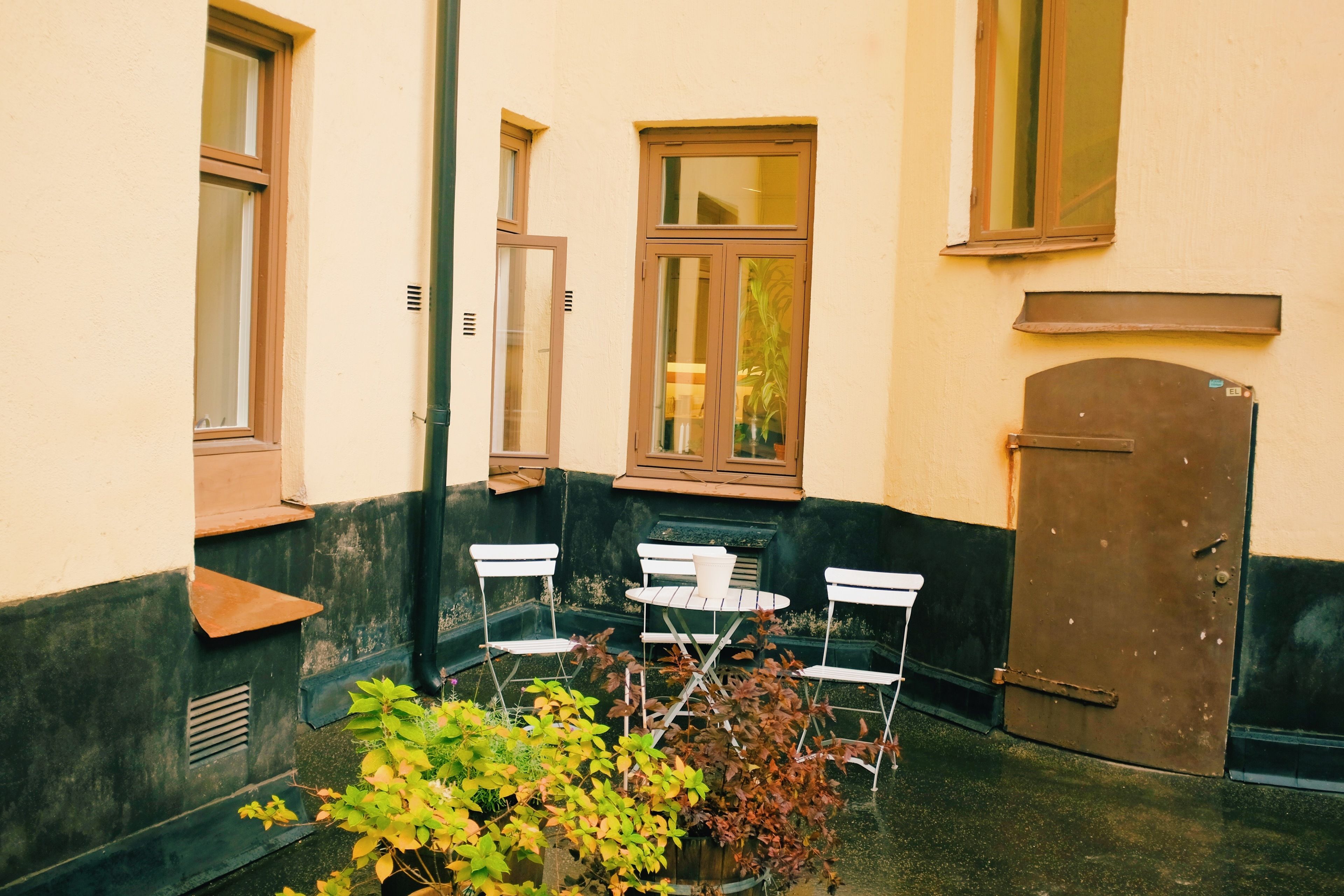A small outdoor seating area with a table and chairs, a potted plant, and a door.